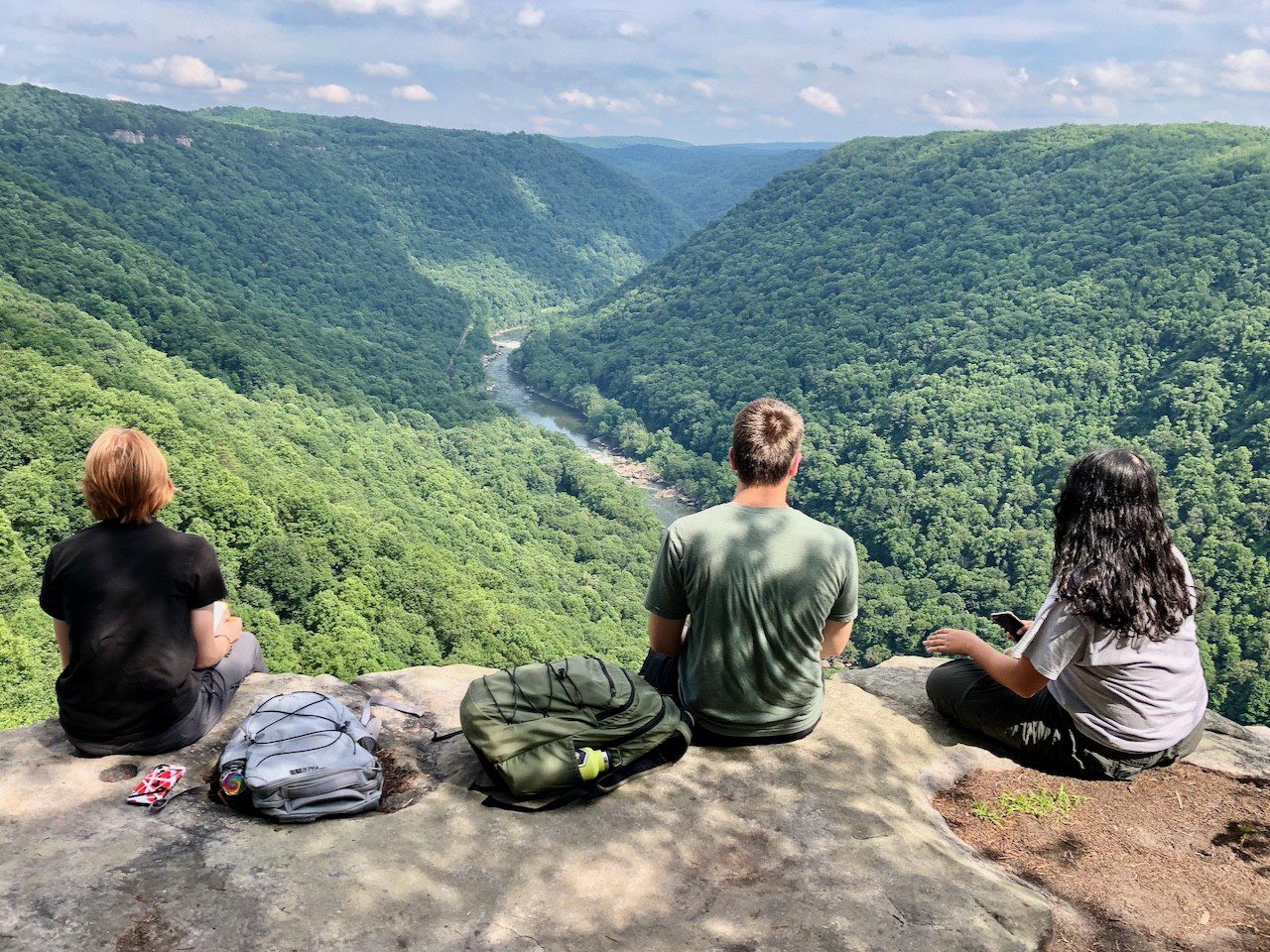 Geoscience students sitting on a cliff overlook, looking down on the West Virginia mountains.