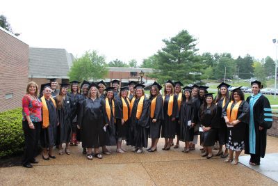 A group of Concord University Early Childhood Regents Bachelor of Arts graduates standing together in their caps and gowns in front of the Art Building