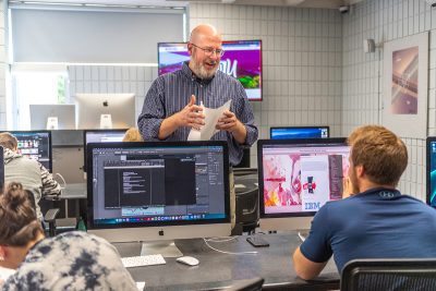 Advertising/Graphic Design students talking to their professor in the CU state-of-the-art Mac Lab