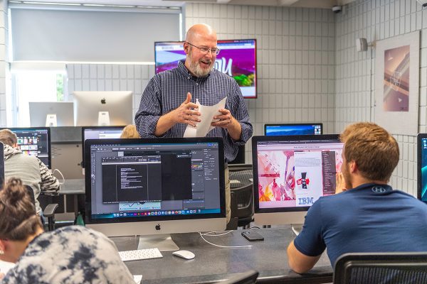 Advertising/Graphic Design students talking to their professor in the CU state-of-the-art Mac Lab