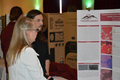 Geology student explaining research from a poster board to a visitor at a Research Festival.