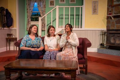 3 CU students wearing floral print costumes sit on a couch on the set of A Bad Year For Tomatoes