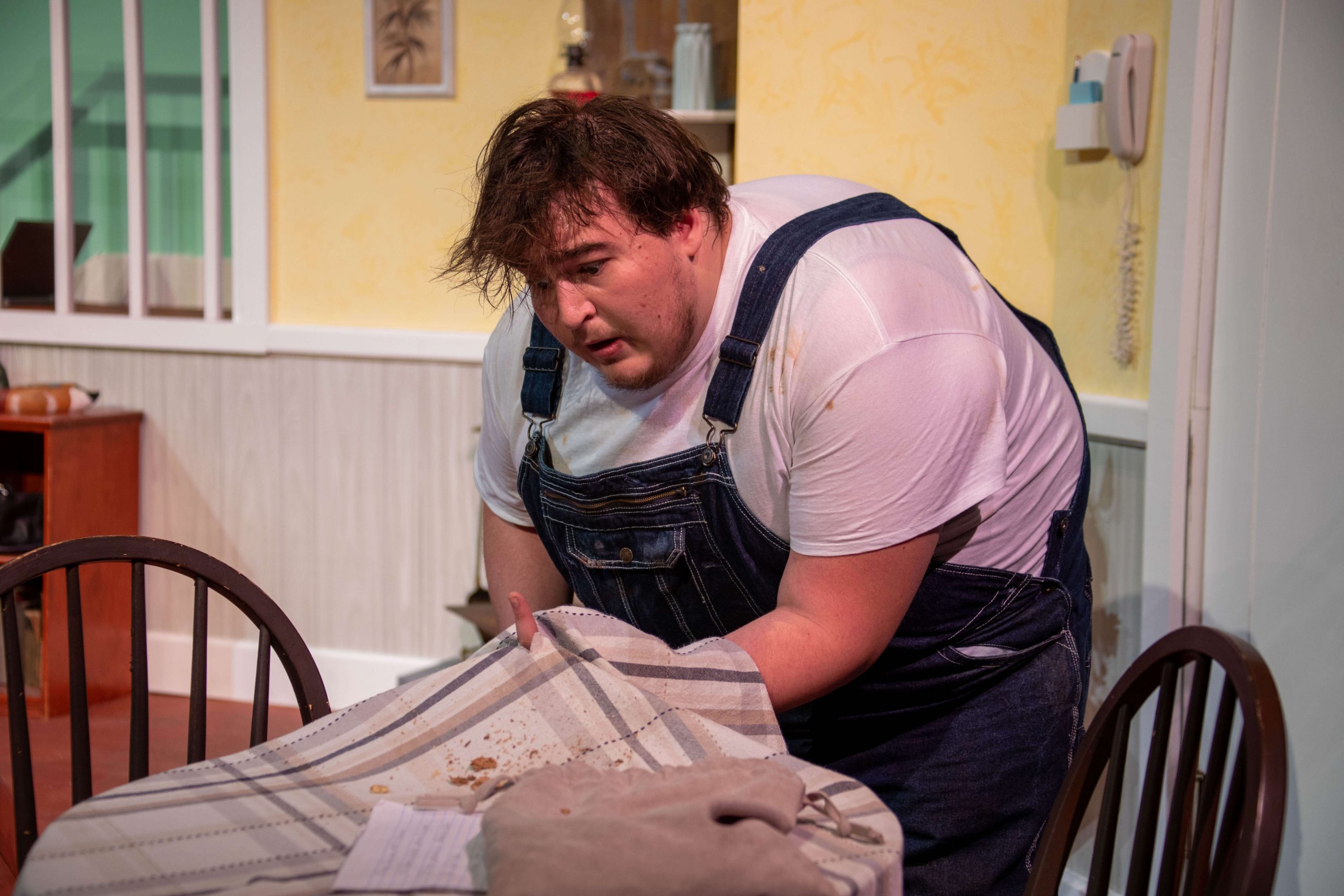 A Concord student performing in A Bad Year For Tomatoes. He is wearing a white t-shirt and overalls, and looks very surprised