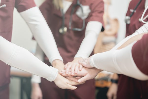 A group of nursing students with their hands joined in a team pose.