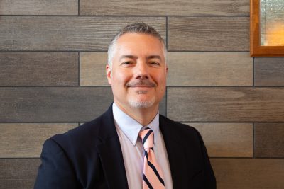 A photo of Andrew Sulgit standing front of a gray slate tile wall.