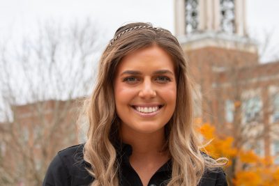 A photo of Lilly Fleming in front of the Concord bell tower against a dark blue moody October sky.