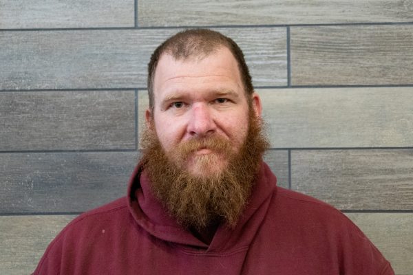 A photo of John Russell standing in front of a gray slate tile wall.