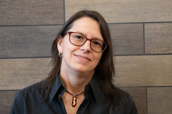 A photo of Kim Nichols standing in front of a gray slate tile wall.