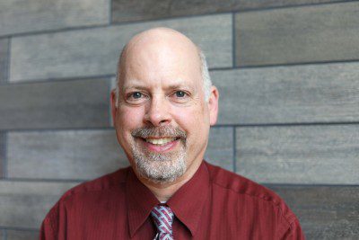 A photo of Jonathan Berkey in front of a gray slate wall