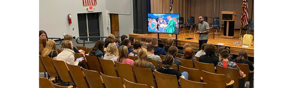 A member of the Student Success Agency speaking with students from Mullens Middle School in their school auditorium