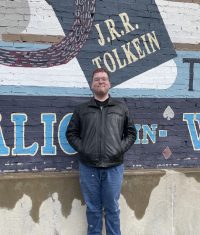 A photo of Michael Simmons standing in front of a mural of books