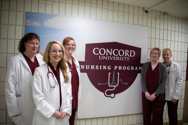Members of the Nursing Department stand together in front of a nursing banner