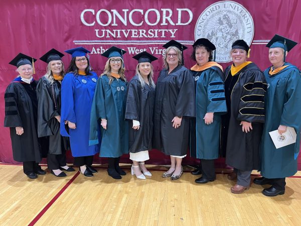 Administration, nursing faculty, and BSN graduates pose in front of a Concord University curtain